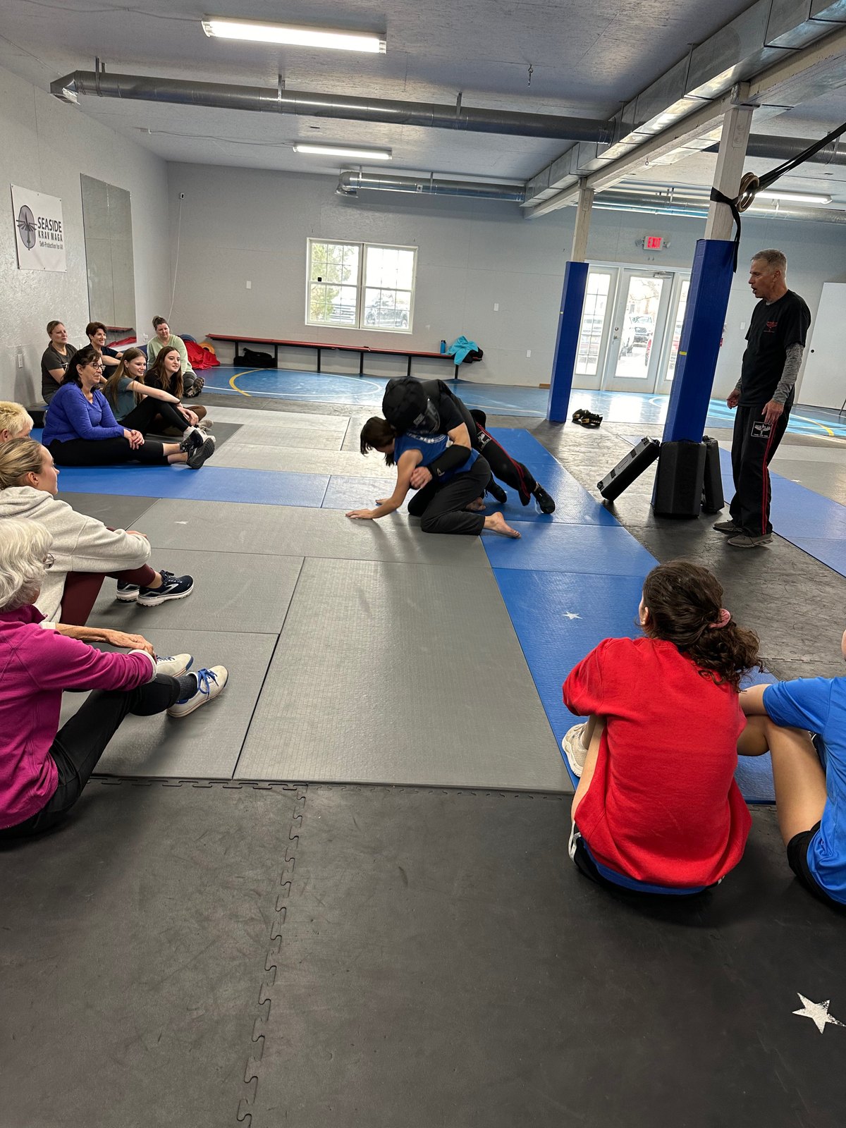 A women's self-defense clinic watching a ground-defense demonstration at Seaside Krav Maga