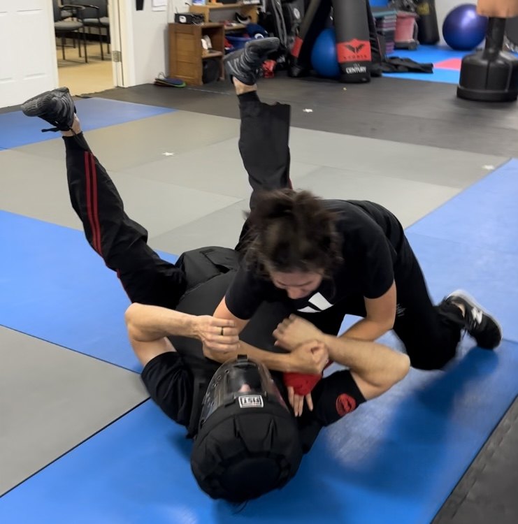 A clinic participant practising a ground-defense escape against a padded attacker